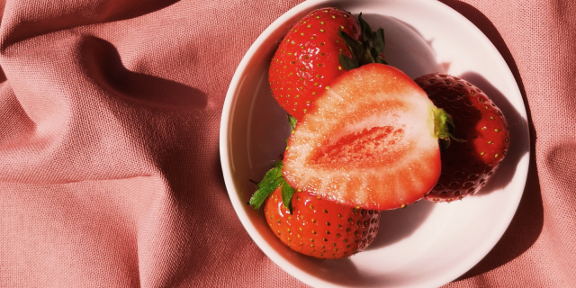 A cut open strawberry in a bowl thats sitting on a pink fabric