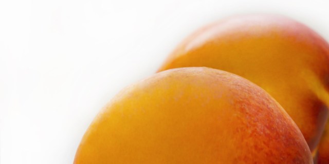 Against a white background, two peaches emerge side by side from the bottom right corner of the image.