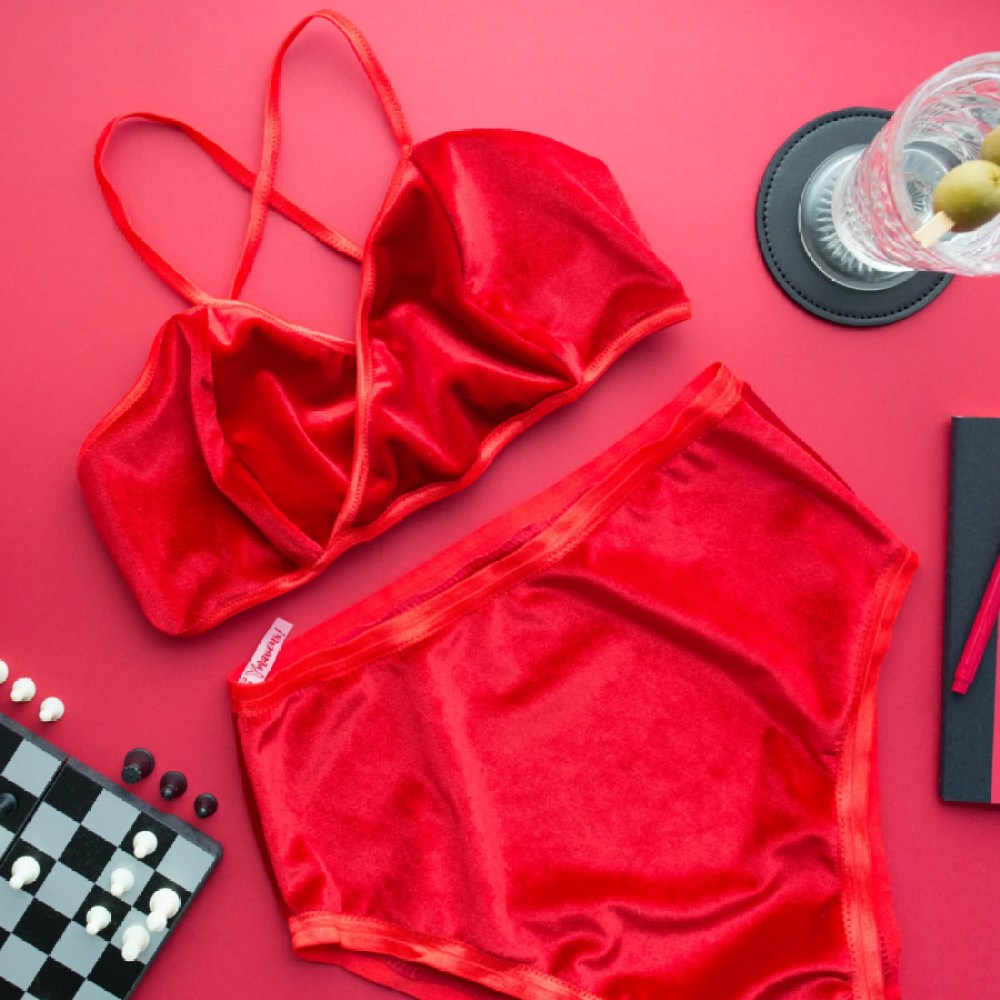 A red velvet soft bra and high waits panties are thrown against a pink background.