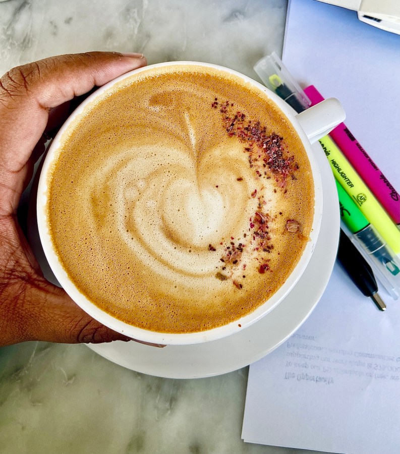 a gorgeous Cocoa Butter Mint Latte held by shea with papers and highlighters on the table in the background