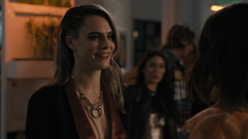 Alice smiles at Mabel wearing an open blazer with nothing underneath and chain necklaces 
