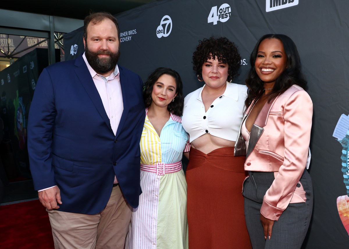 a tall white man in a blue jacket, a dark haired white woman in a rainbow striped dress, a white woman with dark curly hair in a white top and red skirt, a black woman with a pink satin jacket and grey pants