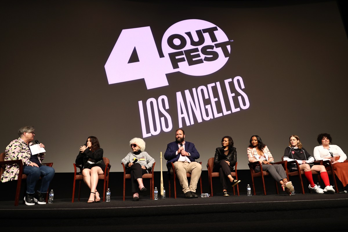 a far away shot of 8 people sitting on a stage. the outfest 40th anniversary logo is largely displayed in the background