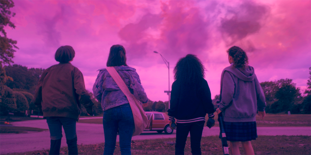 4 teen girls look at a pink hued sky with their backs to the camera