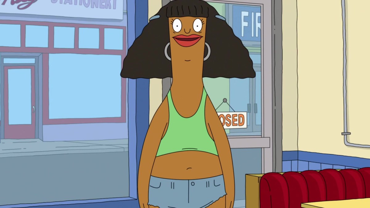 In a still from Bob's burgers, Marshmallow, a Black trans woman with a cut bob hair, is in a green crop top and silver hoops earrings. She is inside Bob's Burgers, with the door behind her.