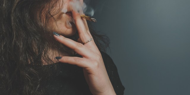 a person with long hair and green nail polish holds a joint up to their mouth, smoking