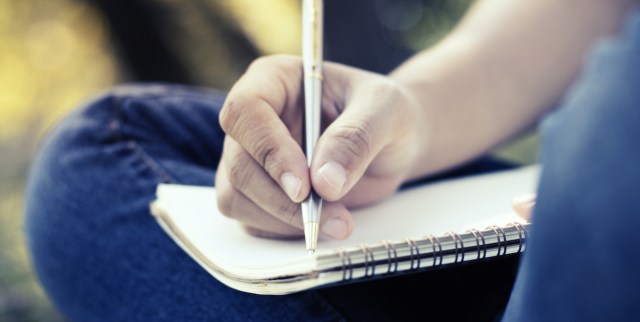 close up of a young person with short fingernails wearing blue jeans and journaling in a spiral notebook