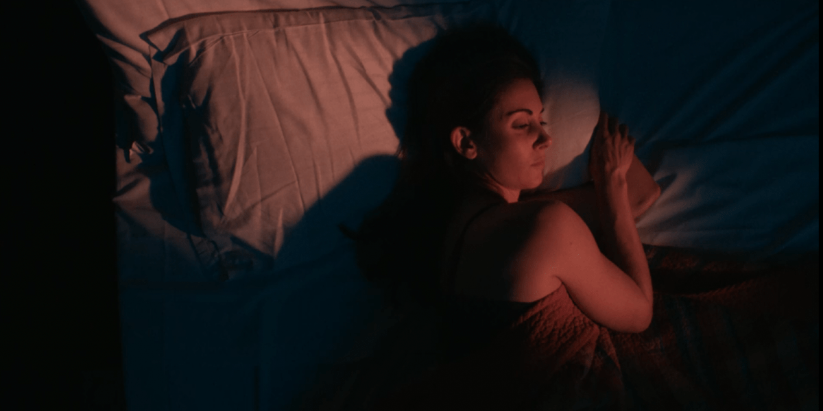 Alison Brie sleeping in a bed with red lighting