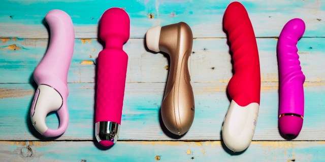 A collection of five pink vibrators of different shapes and sizes, played on a wood table with worn out turquoise paint