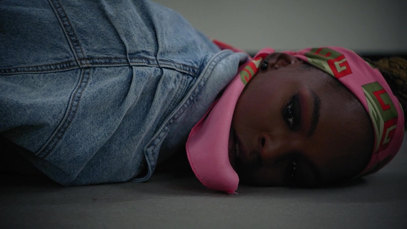 Ness lies on the landing of the courthouse steps after being stabbed. In this show, she's wearing a denim blazer and a pink scarf on her head that drapes over her mouth as she lies on the ground.