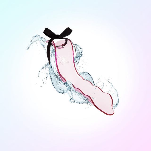 The WaterSlyde, a pink piece of plastic shaped like a slide has a black bow on top, is against a pastel background of pinks, blues, purples and whites. Splashing water is visible around the toy.