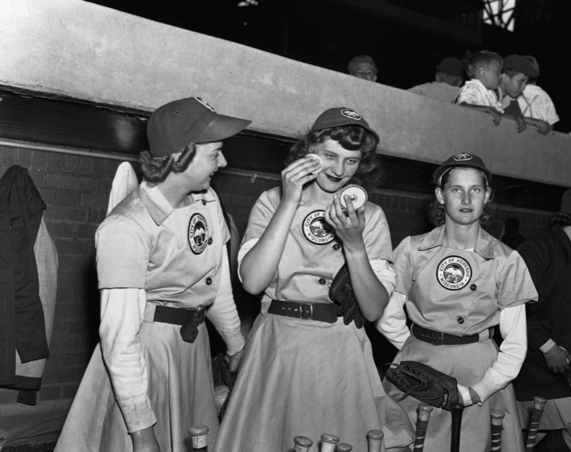 Elise Harney, pitcher for the Kenosha Comets, refreshes her makeup between innings as teammate Janice O'Hara and another player look on. The women of the All-American Girls Professional Baseball League were required to look their best whether on or off the field, and received "charm school" training to teach them how to maintain that feminine look.