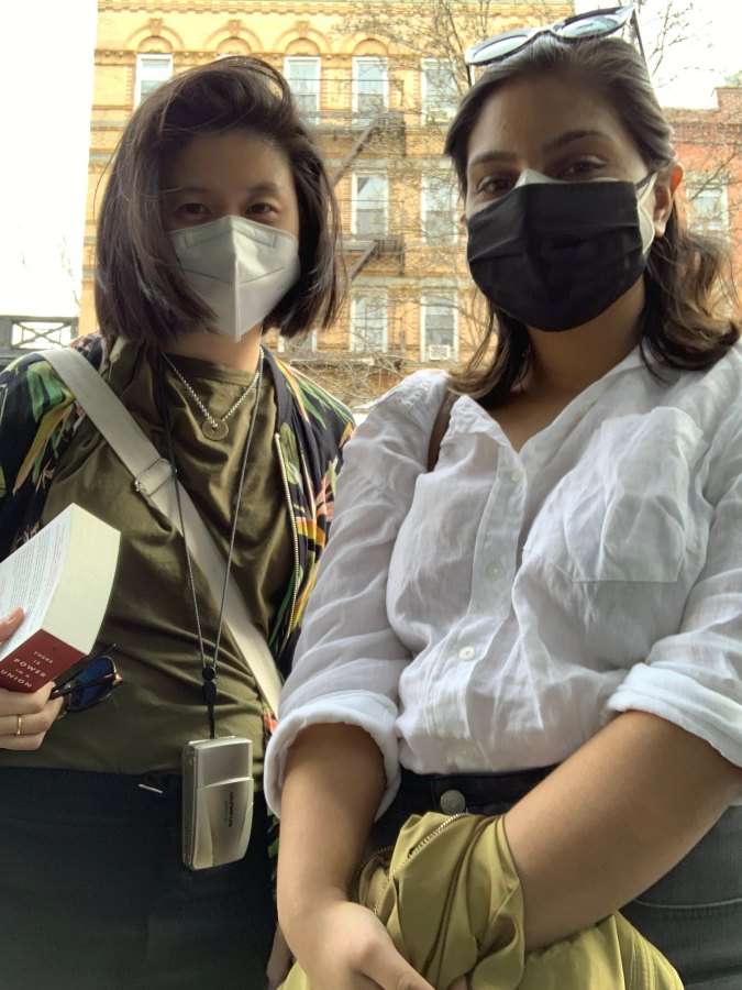 Gerrie and Ashni pose for a photo while wearing masks. They are outdoors and look like they are on their way somewhere with bags on their shoulders and such
