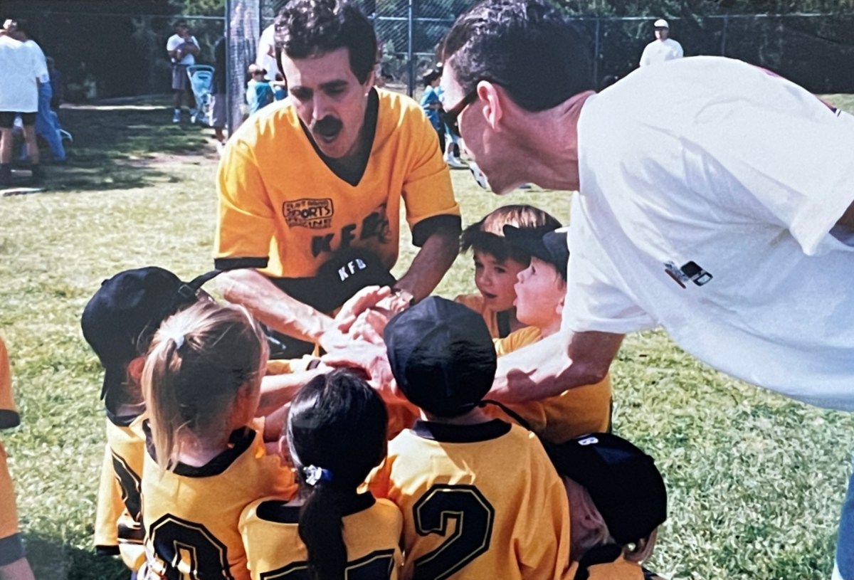 A group of kids in soccer uniforms gather around their coaches.