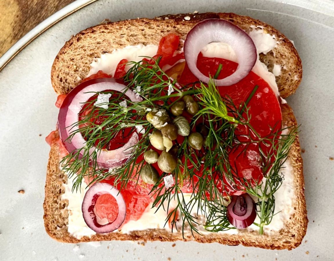 An open-faced sandwich with red onion, smoked salmon, tomato, capers, and dill