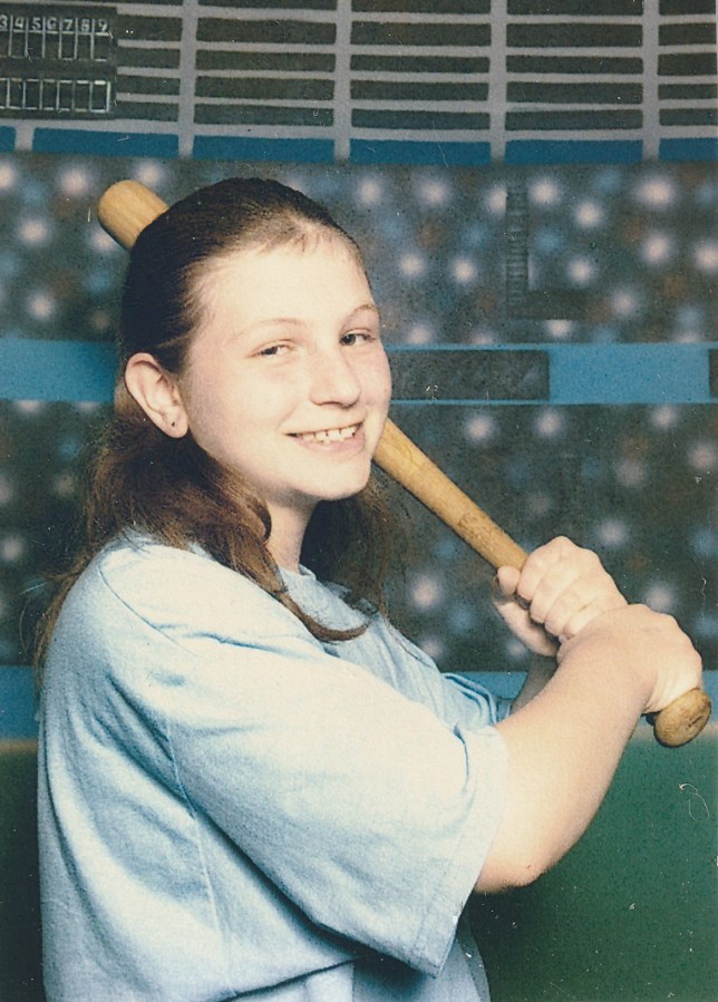 Katie Reilly as a young child holds a baseball bat while posing for a photo