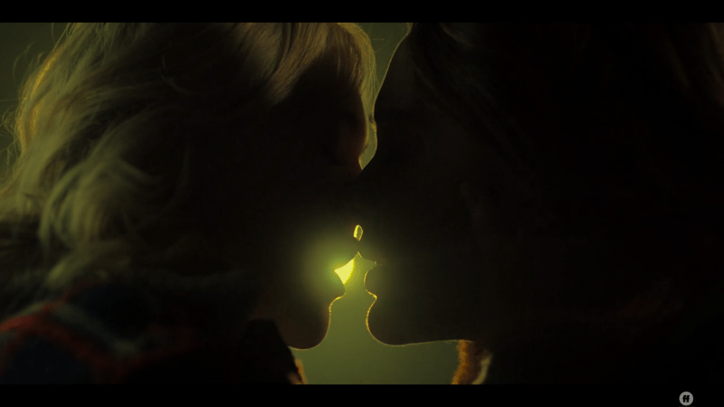 Raelle and Scylla kiss, backlit by the stage lights