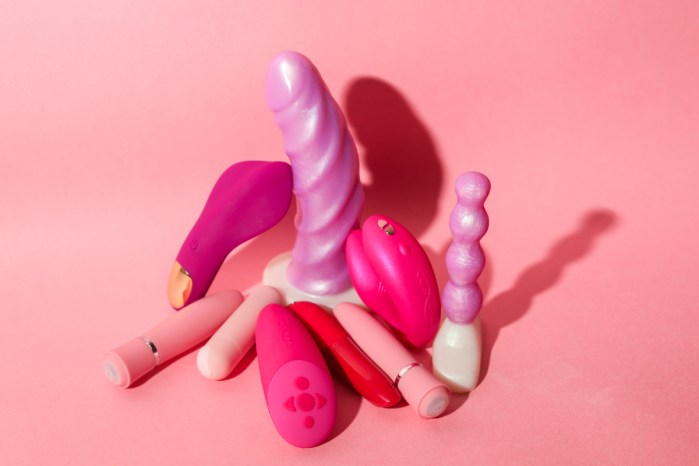 several pink and purple sex toys of various shades are seen here pictured against a peachy pink background