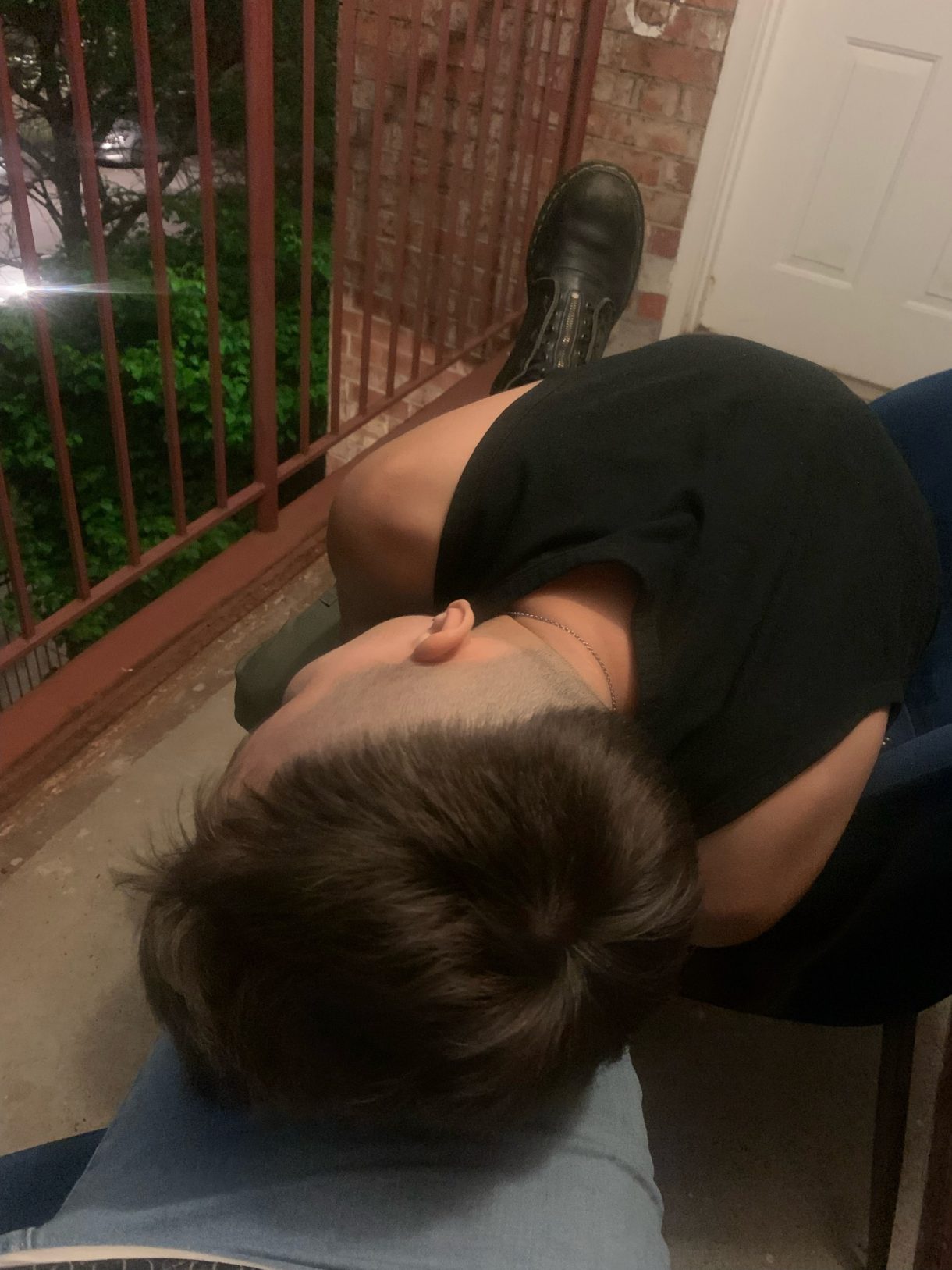 Ro is here seen from behind taking a rest on someone else's leg. Ro is a white person with a short haircut wearing a black sleeveless tee.