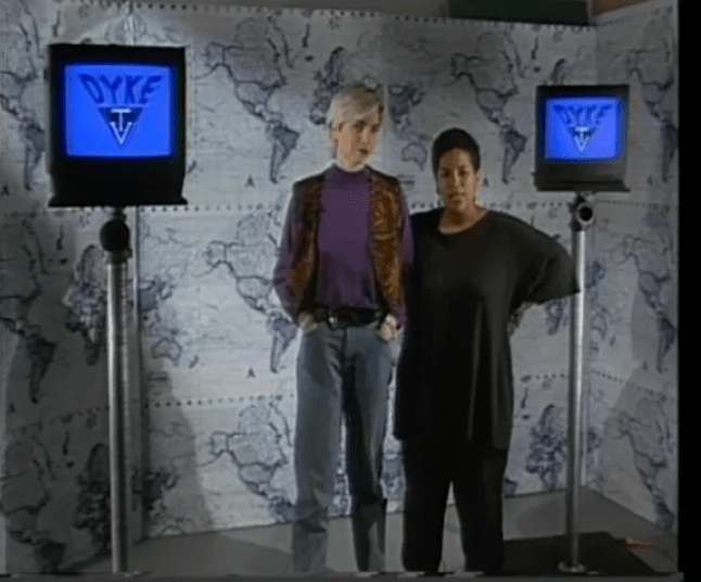 A white woman and a Black woman stand next to each other during the opening segment of Dyke TV with monitors behind them that say Dyke TV
