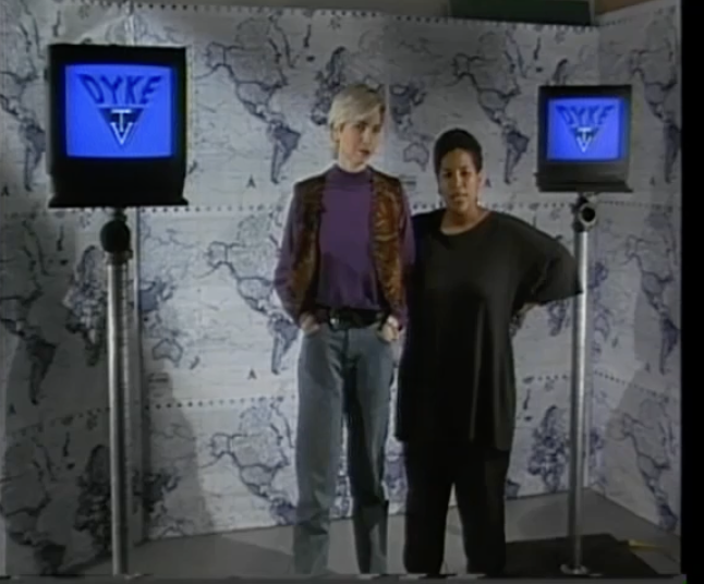 A white woman and a Black woman stand next to each other during the opening segment of Dyke TV with monitors behind them that say Dyke TV