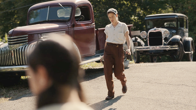 Jess walks down the road carrying Coke bottles. 