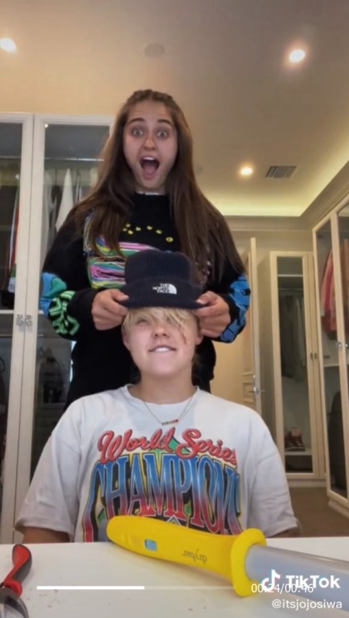Avery Cyrus putting a beanie onto JoJo Siwa's head, her mouth open with excitement