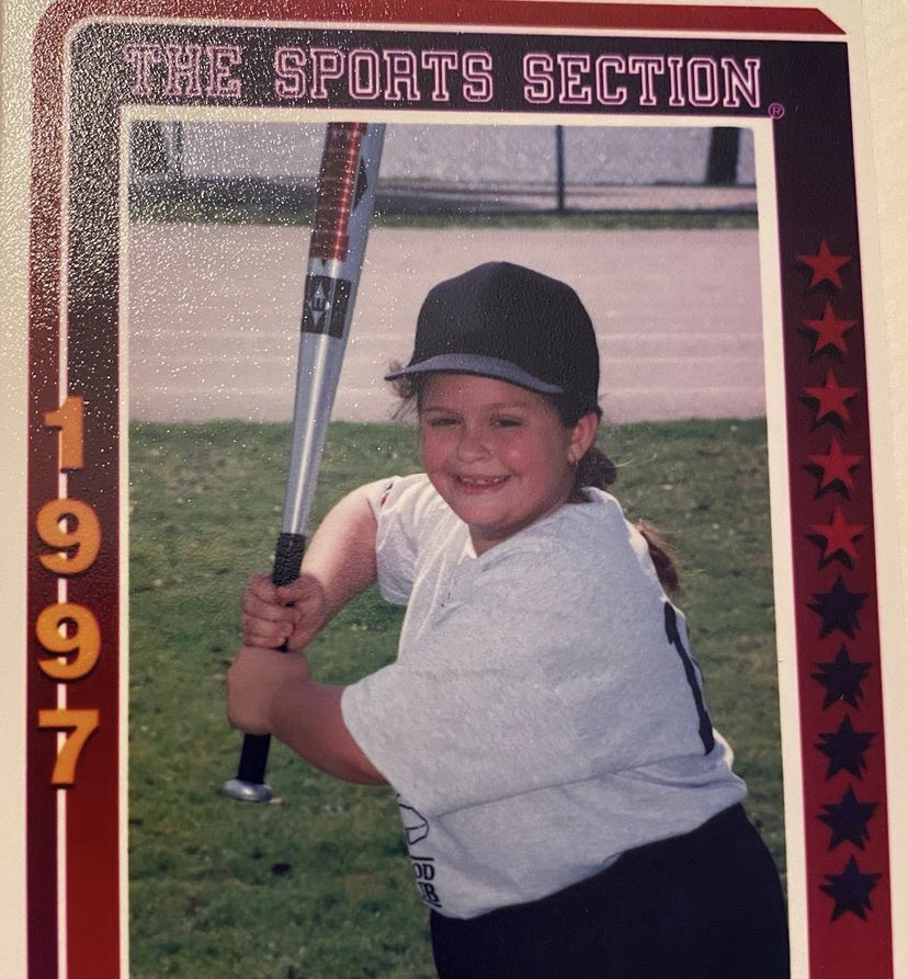 Stef Rubino as a child holds a baseball bat while posing for a photo. The border says The Sports Section 1997