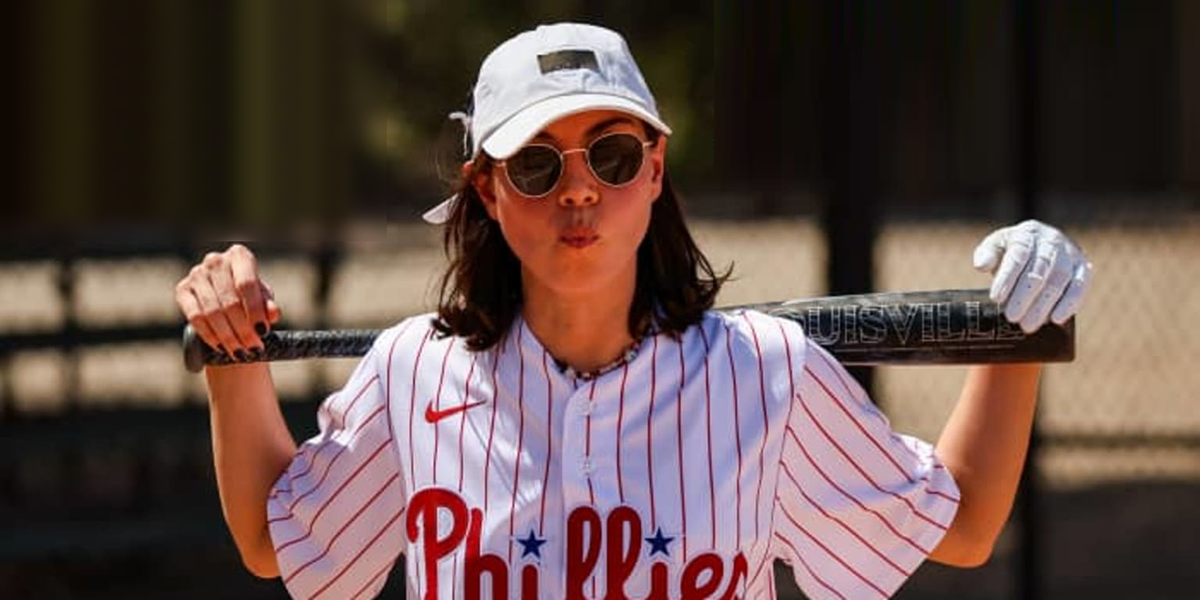 Aubrey Plaza in a Phillies baseball jersey with a bat slung over her shoulders