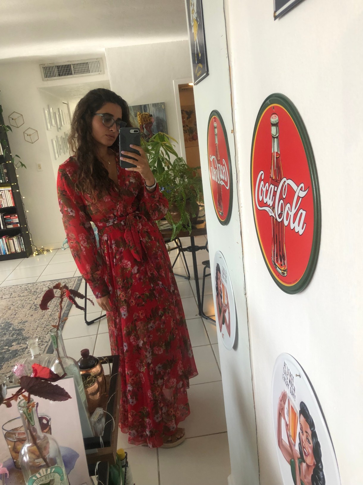 Kayla Kumari Upadhyaya is wearing a long floral v-neck dress and wedge sandals.