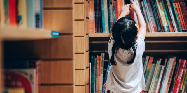 Little Asian girl choosing books from the bookshelf in library