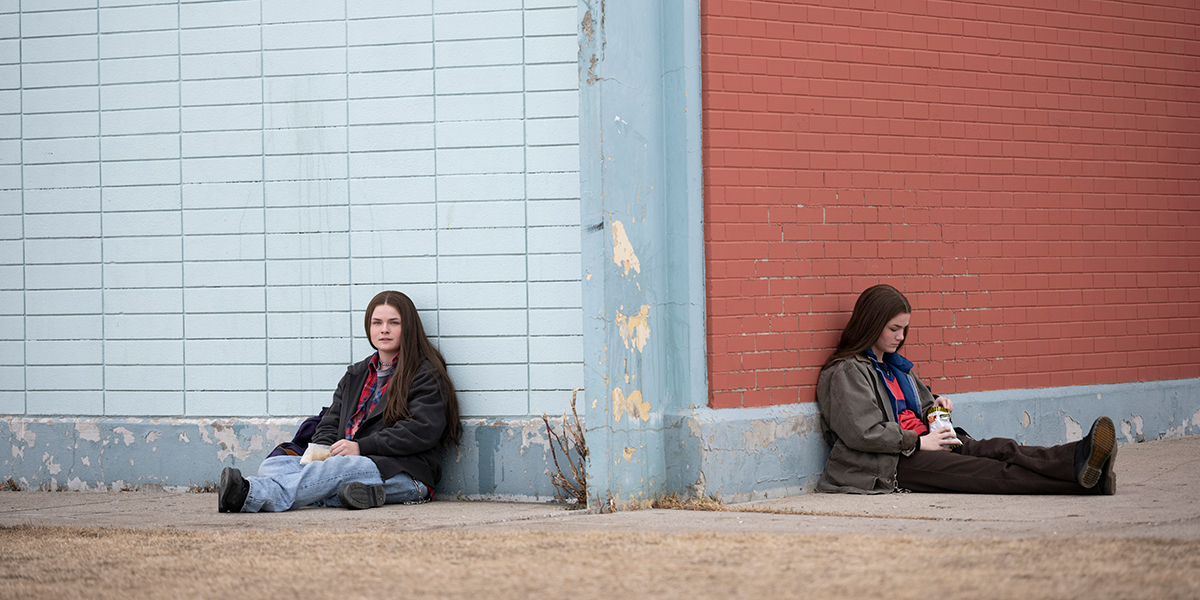 Railey and Seazynn Gilliland as Tegan and Sara Quinn lie against perpendicular ends of the same school building.