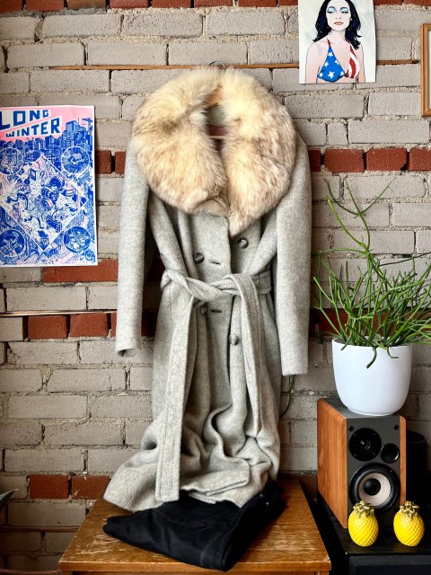 a brick wall, with a picture of PJ Harvey in the upper right corner and a power that says Long Winter in the left.  Hanging on the wall is a long gray jacket with a fur collar