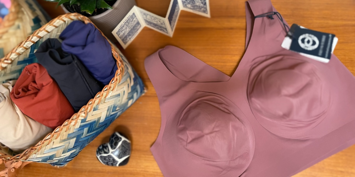 An image of a lavender bra sitting on a wooden table. More bras in various colors are rolled up in a blue and white basket beside it.