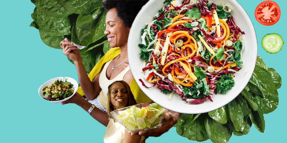 Two Black women eat salads while smiling. There's a large bowl of salad and leafy greens surrounding them.