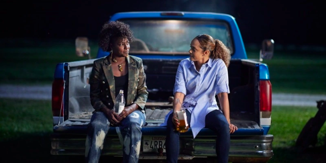 Nova and Billie sit on the back of an old blue pickup truck, sipping out of 40 oz bottles, talking about their day.