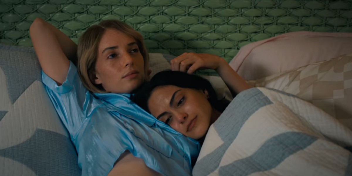 Maya Hawke and Camila Mendes in Do Revenge lay in a bed together, snuggling.