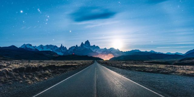 A wide open road leading toward mountains set against a night sky