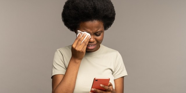 young Black woman looking at a cell phone, reading text messages, and crying