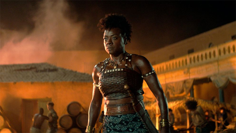 Viola Davis dressed as a Dahomey warrior in front of an orange sky in The Woman King