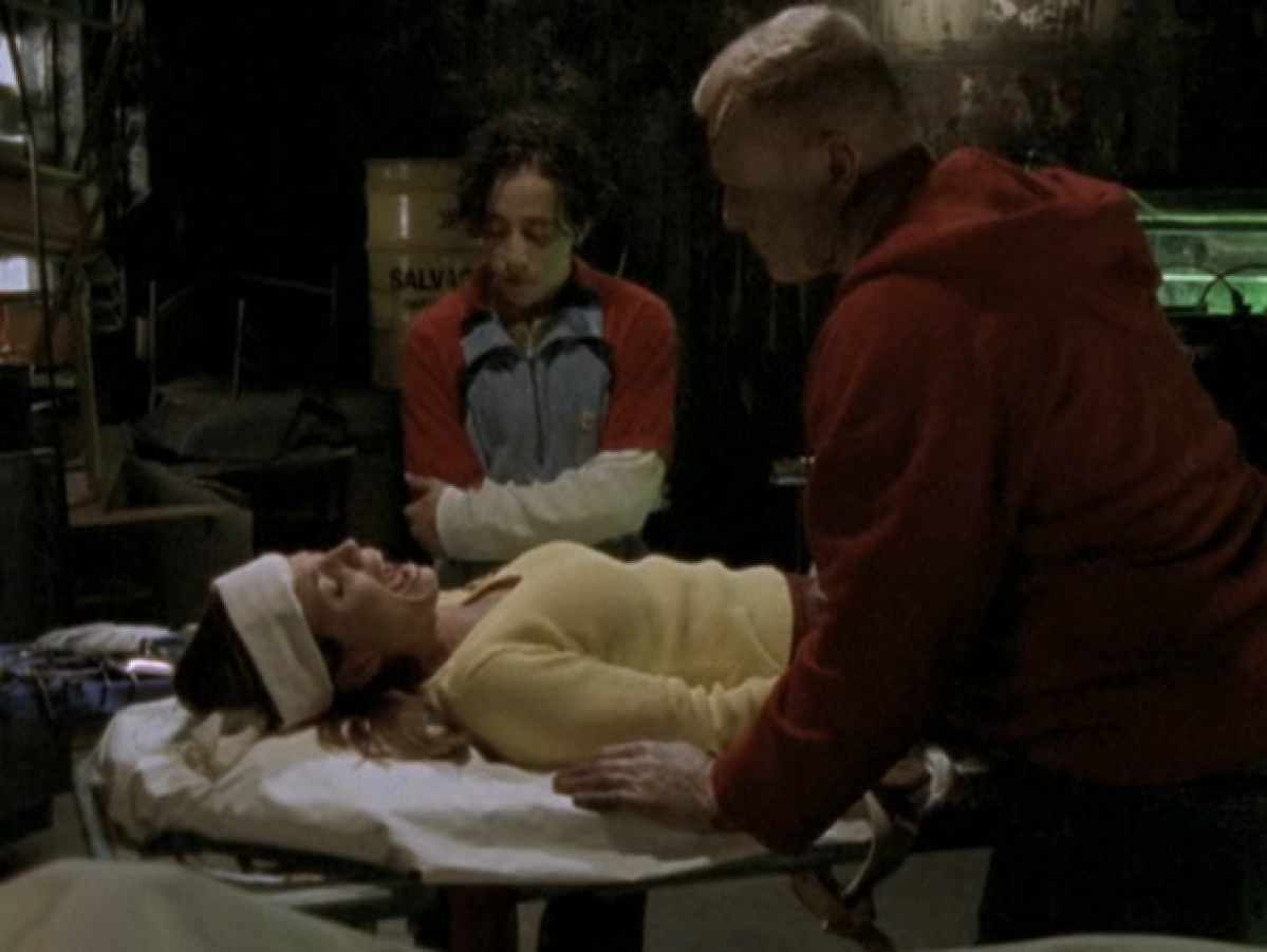 Cordelia lies on a platform, screaming, as two high school boys hover over her.