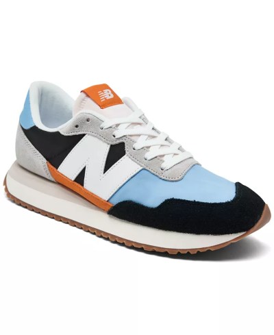 Light blue and navy New Balance shoes have a white N on the side and orange detail marks at the arc of the foot and the tongue, it's tied together with white shoelaces.