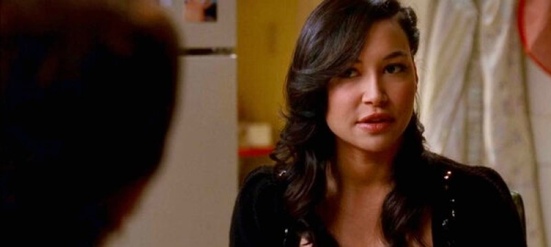 Santana Lopez looks at her grandmother (off camera) from their kitchen table, her hair is swept to the side.
