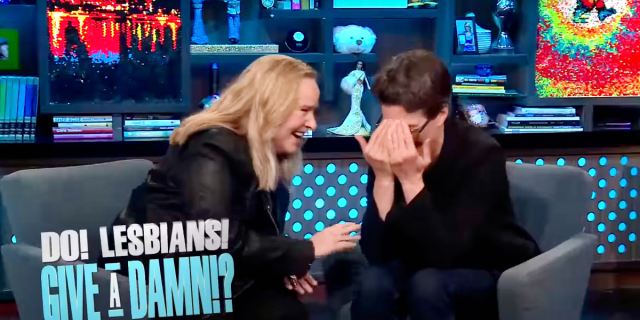 Rachel Maddow and Melissa Etheridge laugh together while sitting close in chairs on Andy Cohen's set for "Watch What Happens Live," super imposed beneath them in block letters are the words "Do Lesbians Give a Damn"