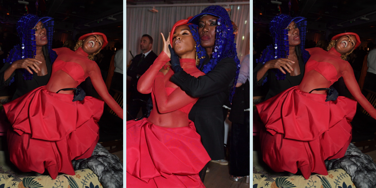 Grace Jones and Janelle Monáe goof off on the red carpet for Glass Onion: A Knives Out Mystery. Janelle wears a red dress and red hat, and Grace wears a black blazer, gloves, and sparkly blue headpiece