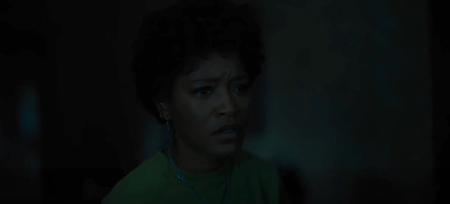 Keke Palmer shrouded in darkness wearing a lime green top looks off in horror.