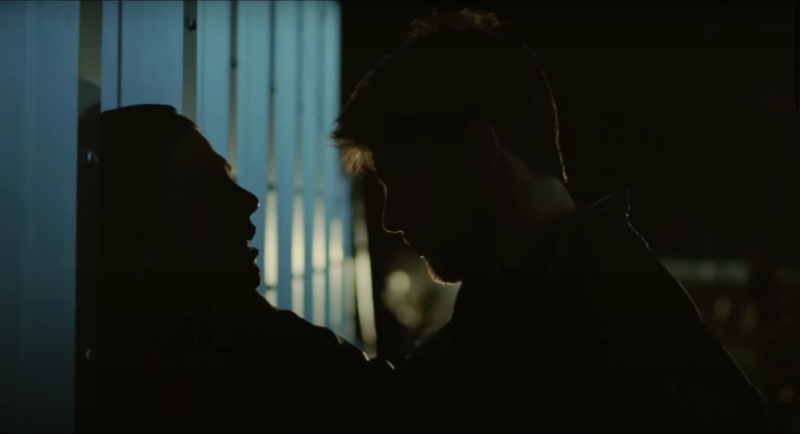 A backlit image of one man holding another up against a wall by his throat.