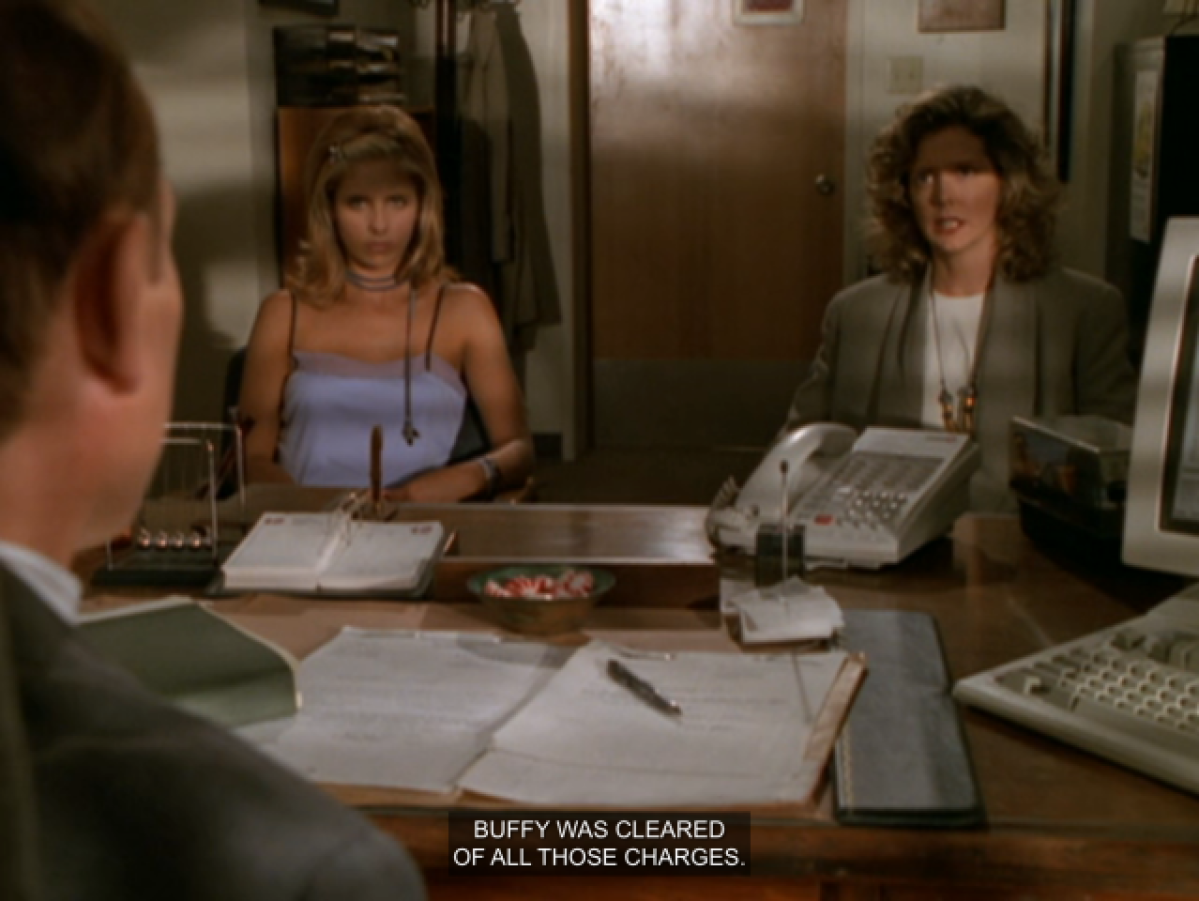 Buffy wearing a purple spaghetti strap top, sitting with Joyce in Principal Snyder's office.  Joyce says "Buffy was cleared of all these charges."