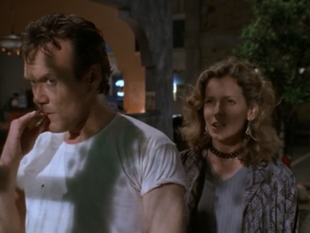 Giles wearing a plain t-shirt with the sleeves rolled up, sucking on a cigarette. Joyce next to him, wearing a choker