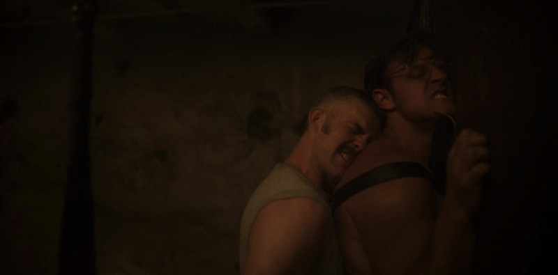 Russell Tovey presses a man against a wall while fucking him in a dark basement. 